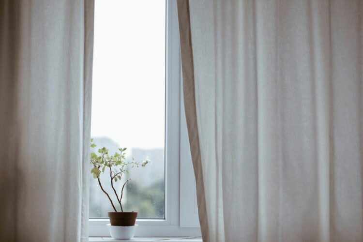 Finestra aperta con tende chiare e luce di primavera: pulizie di primavera
